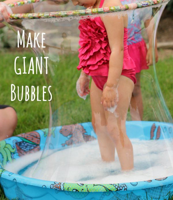 A little girl is standing in a kiddie pool. A hula hoop surrounds her and a giant bubble. (preschool science)