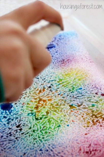 A child's hand is shown in front of a bright colored wax paper drawing.